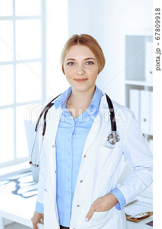 Young woman doctor at work in hospital looking at camera. Blue colored blouse of therapist looks good. Medicine and healthcare concept Young woman doctor at work in hospital looking at camera. Blue colored blouse of therapist looks good. Medicine and healthcare concept 67809918