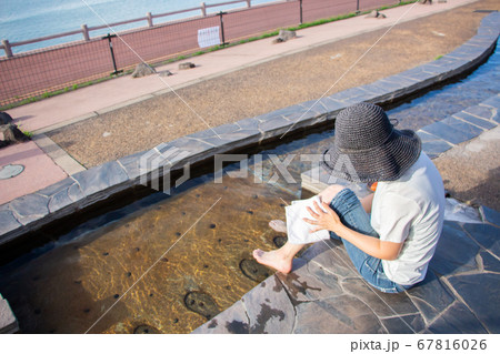 鹿児島県垂水市の道の駅、湯っ足り館の足湯で足を拭く女性 白いシャツと黒い帽子の女性 鹿児島県垂水市の道の駅、湯っ足り館の足湯で足を拭く女性 白いシャツと黒い帽子の女性 67816026