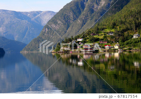 ノルウェー ハダンゲルフィヨルド、ウルヴィク地区、朝日に照らされた家々と早朝の山々と水面の風景を望む ノルウェー ハダンゲルフィヨルド、ウルヴィク地区、朝日に照らされた家々と早朝の山々と水面の風景を望む 67817554