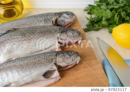 Close-up of three raw gutted trout fishes on a wood cutting board prepared for cooking. Close-up of three raw gutted trout fishes on a wood cutting board prepared for cooking. 67823117