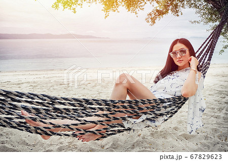 Beautiful woman sitting on a swing on the beach Beautiful woman sitting on a swing on the beach 67829623