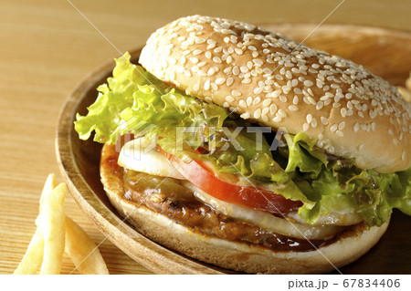 丸い木皿の上のテリヤキバーガーとこぼれ落ちるポテトフライ 丸い木皿の上のテリヤキバーガーとこぼれ落ちるポテトフライ 67834406