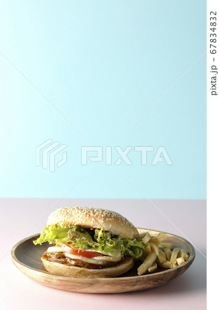 ピンクと水色の2色の背景紙を使って撮影した木皿の上のテリヤキバーガーとポテトフライ 67834832