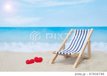 Two red hearts and deck chair on white sand beach with blurred blue sea and sky Two red hearts and deck chair on white sand beach with blurred blue sea and sky 67836786