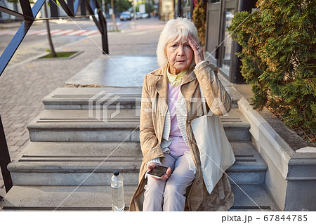 Sad woman with bottle of water sitting on the steps near the building Sad woman with bottle of water sitting on the steps near the building 67844785