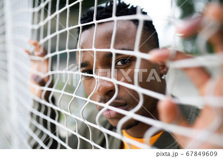 Frustrated young black man behind net outdoors in city, black lives matter concept. Frustrated young black man behind net outdoors in city, black lives matter concept. 67849609