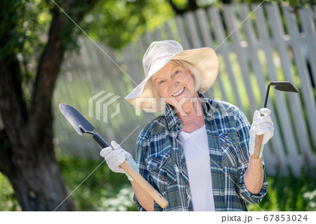 Elderly woman holding a rake and a hoe Elderly woman holding a rake and a hoe 67853024