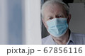 Portrait of sad grandfather in medical mask looks at camera anxiously at home 67856116
