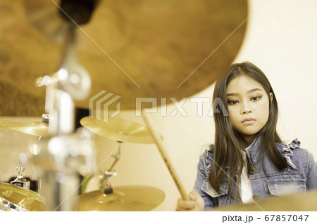 A cute Asian elementary school girl with long hair playing drums  67857047