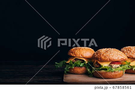 three homemade hamburgers with meat, cheese, lettuce, tomato on a wooden Board on a table on a black background 67858561