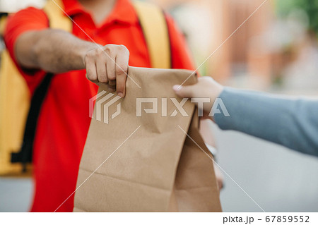 Give order to client in town. Deliveryman in uniform with yellow backpack holds paper bag Give order to client in town. Deliveryman in uniform with yellow backpack holds paper bag 67859552