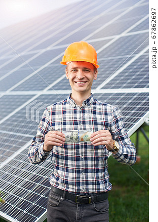 Smiling man with hundred dollar bill in hand shows thumb a sign like at the background of solar station Smiling man with hundred dollar bill in hand shows thumb a sign like at the background of solar station 67862697