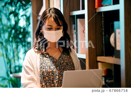 オフィスの本棚の前でデスクワークするマスクの若い女性 67866758