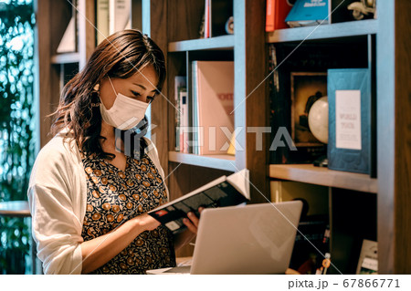 オフィスの本棚の前でデスクワークするマスクの若い女性 オフィスの本棚の前でデスクワークするマスクの若い女性 67866771