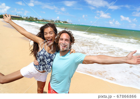 Happy people jumping screaming of fun on beach summer vacation travel in Hawaii. Laughing young Asian woman with Caucasian man, tourists couple friends on holiday Happy people jumping screaming of fun on beach summer vacation travel in Hawaii. Laughing young Asian woman with Caucasian man, tourists couple friends on holiday 67866866