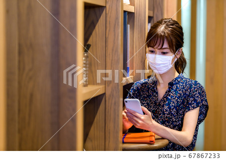 オフィスでスマホを操作するカジュアル衣装のマスクをした若い女性 オフィスでスマホを操作するカジュアル衣装のマスクをした若い女性 67867233