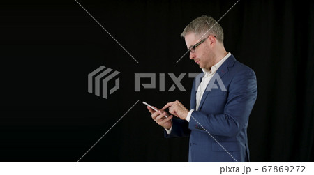 Businessman taps on his smartphone on black background Businessman taps on his smartphone on black background 67869272