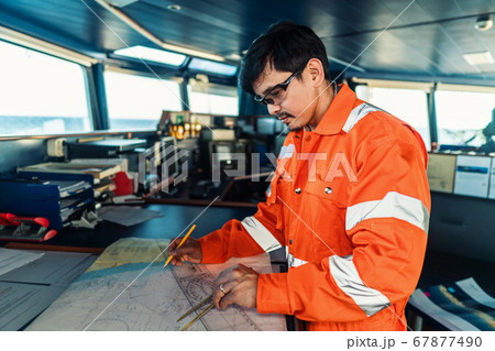 Filipino deck Officer on bridge of vessel or ship. He is plotting position on chart 67877490