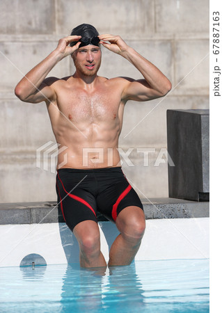 Swimmer athlete getting ready preparing for race putting on goggles glasses and cap for swim race competition at indoor swimming pool stadium. Young man in shorts his 20s 67887163