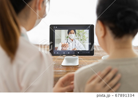 オンライン診療を受けるシニア女性とそのケアスタッフ、及び通話アプリで繋がっている医師 67891334