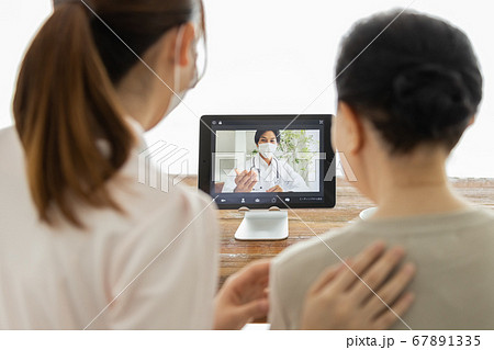 オンライン診療を受けるシニア女性とそのケアスタッフ、及び通話アプリで繋がっている医師 67891335