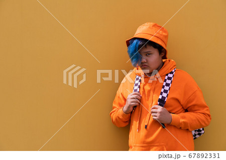 Back to school. A teenage girl with blue hair in an orange hoodie, a Panama hat with a backpack. A high school kid. Back to school. A teenage girl with blue hair in an orange hoodie, a Panama hat with a backpack. A high school kid. 67892331