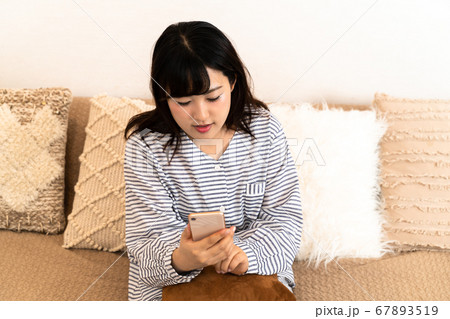 パジャマ姿でスマホを確認する若い主婦 67893519