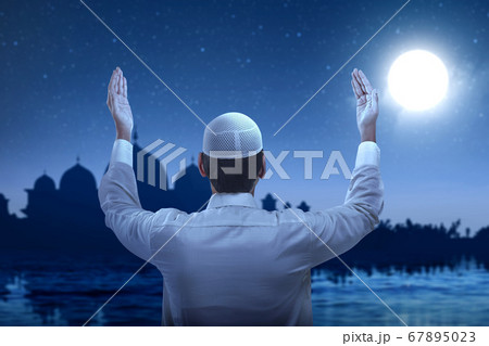Rear view of Asian Muslim man standing while raised hands and praying 67895023