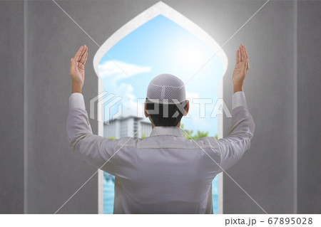 Rear view of Asian Muslim man standing while raised hands and praying 67895028