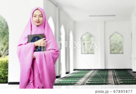 Asian Muslim woman in a veil standing and holding the Quran 67895877