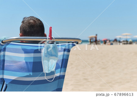 mask and man sitting in a deck chair on the beach mask and man sitting in a deck chair on the beach 67896613