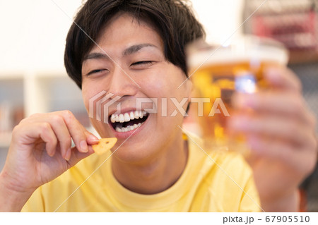 オンライン飲み会　スナックを食べながらビールを飲む若い男性のアップ 67905510