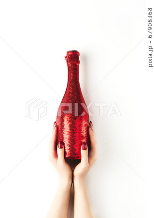 Beautiful female hands with trendy red manicure holding champagne bottle in cover spangled with vibrant red sequines on white background. Mockup for your design. Copy space. Flat lay. 67908368