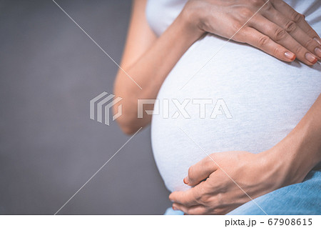 Pregnant woman holds hands on belly on a gray background. pregnancy, motherhood, people and Pregnant woman holds hands on belly on a gray background. pregnancy, motherhood, people and 67908615