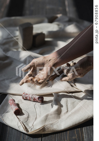 Hands stained in clay going to take cut tool from wooden table, art therapy concept 67908856