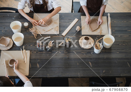 Top view of female hands sculpting different clay products. Big wooden table with pottery tools on a workshop. Top view of female hands sculpting different clay products. Big wooden table with pottery tools on a workshop. 67908870