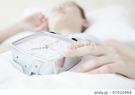 目覚まし時計を持って眠る女性 67910968