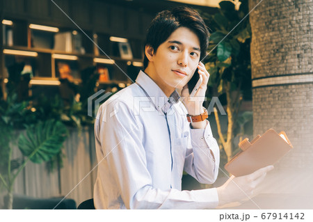 スケジュール帳を見ながら電話をする若い男性 67914142
