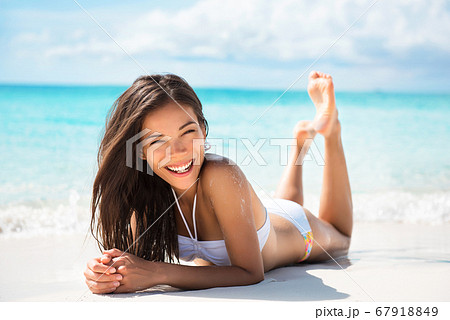 Happy healthy beautiful Asian multiracial woman lying down on sand enjoying sun tanning sunbathing in swimsuit relaxing on Caribbean tropical beach summer vacation. Smiling laughing girl Happy healthy beautiful Asian multiracial woman lying down on sand enjoying sun tanning sunbathing in swimsuit relaxing on Caribbean tropical beach summer vacation. Smiling laughing girl 67918849