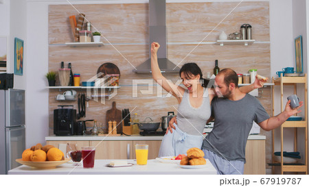 Carefree couple dancing and singing in kitchen Carefree couple dancing and singing in kitchen 67919787
