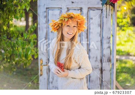 Outdoors lifestyle close up portrait of charming blonde young woman wearing a wreath of autumn leaves. Wearing stylish knitted pullover. Wreath of maple leaves 67923307
