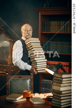 Elderly writer holds stack of books in home office 67927220