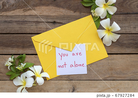 you are not alone message card handwriting in yellow envelope with flowers frangipani arrangement flat lay postcard style 67927284
