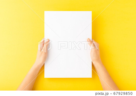Young woman hands showing blank paper sheet on yellow desktop. Top view 67929850