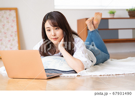 リビングで寝転がりながらノートパソコンを見る若い女性 67931490