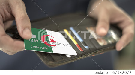 Man pulls plastic bank card with flag of Algeria out of his wallet, fictional card number Man pulls plastic bank card with flag of Algeria out of his wallet, fictional card number 67932072
