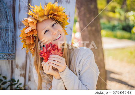 Outdoors lifestyle close up portrait of charming blonde young woman wearing a wreath of autumn leaves. Wearing stylish knitted pullover. Wreath of maple leaves 67934548