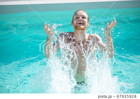 Young cheerful man in pool water splashing with water 67935928