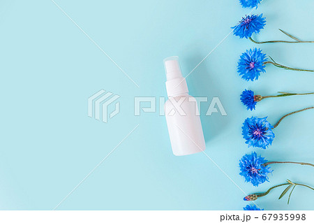 Top view and close-up of unbranded white plastic spray bottle mockup and Flower line of blue cornflowers on a pastel blue background. Natural organic spa cosmetics and liquid antimicrobial spray 67935998