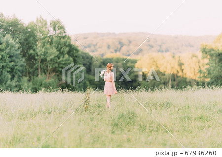 Beautiful young Caucasian blond woman in light dress holding bouquet of white peonies, walking in summer field or garden in sunset. Woman with flowers outdoors 67936260